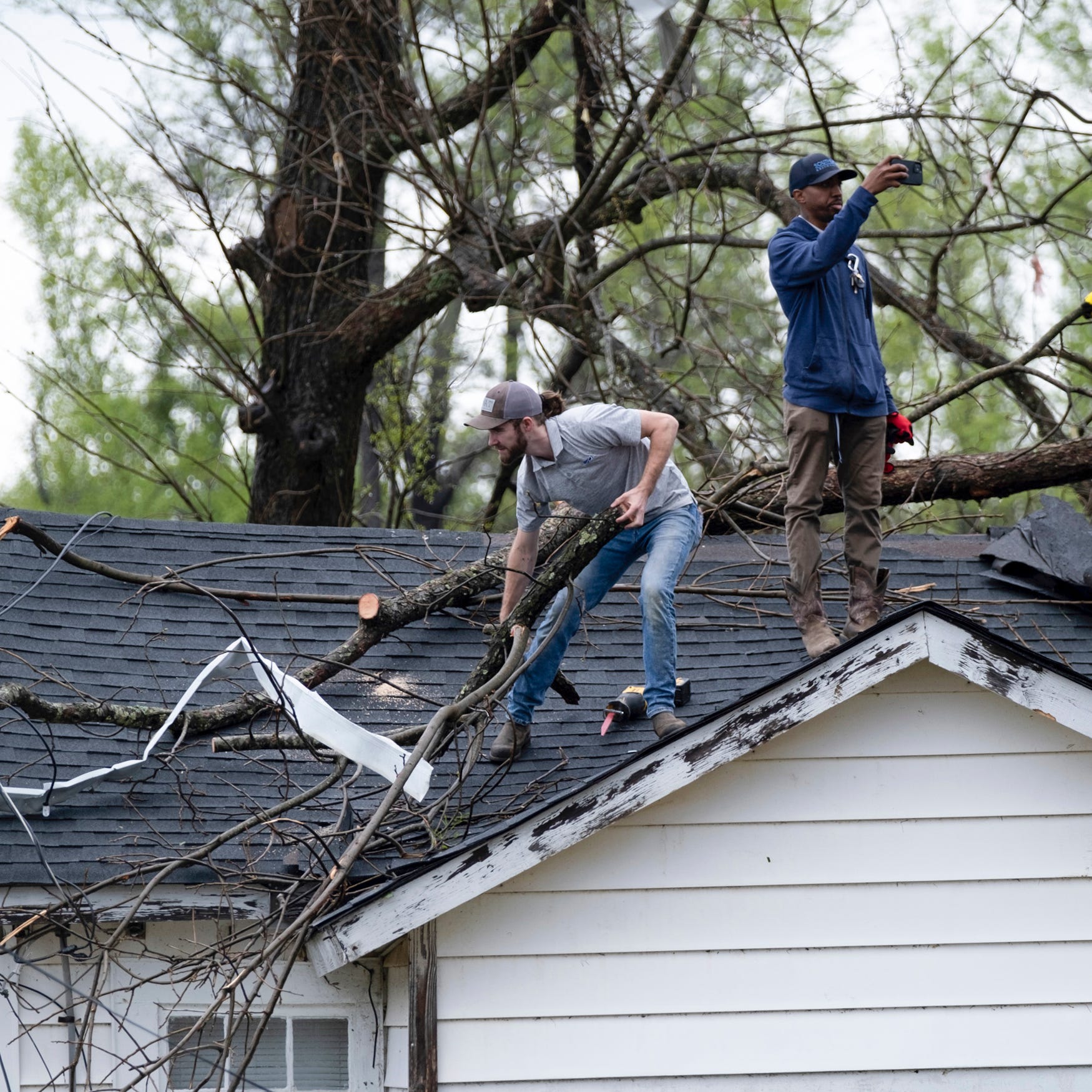 Men clear tree branches off a rooftop on Monday, March 27, 2023, after a tornado ripped through the area the day before, in West Point, Ga. (Ben Gray/Atlanta Journal-Constitution via AP) ORG XMIT: GAATJ113