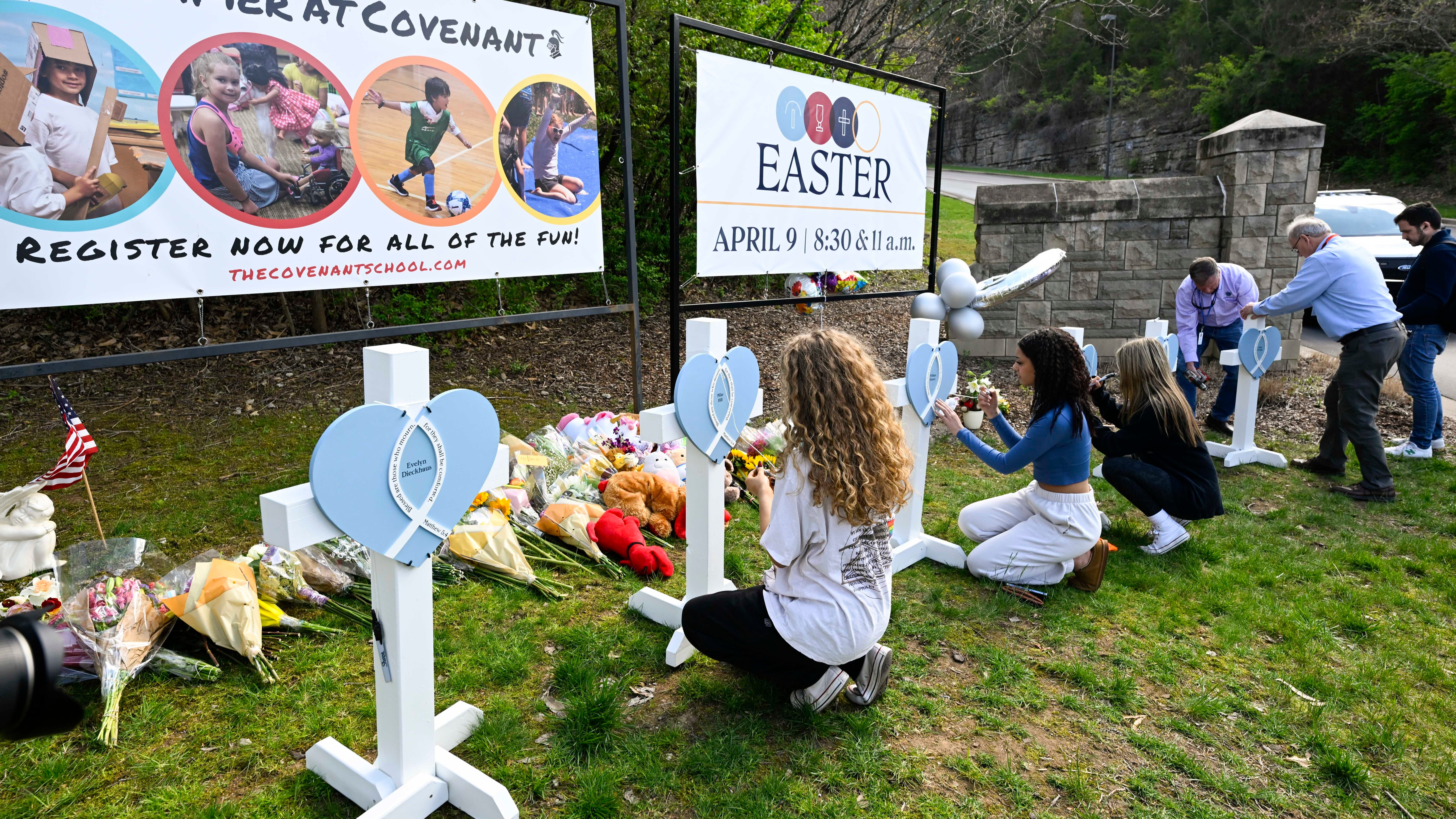 People are pictured writing messages on crosses at an entry to Covenant School in Nashville, Tennessee, which has become a memorial for the victims of Monday's school shooting.