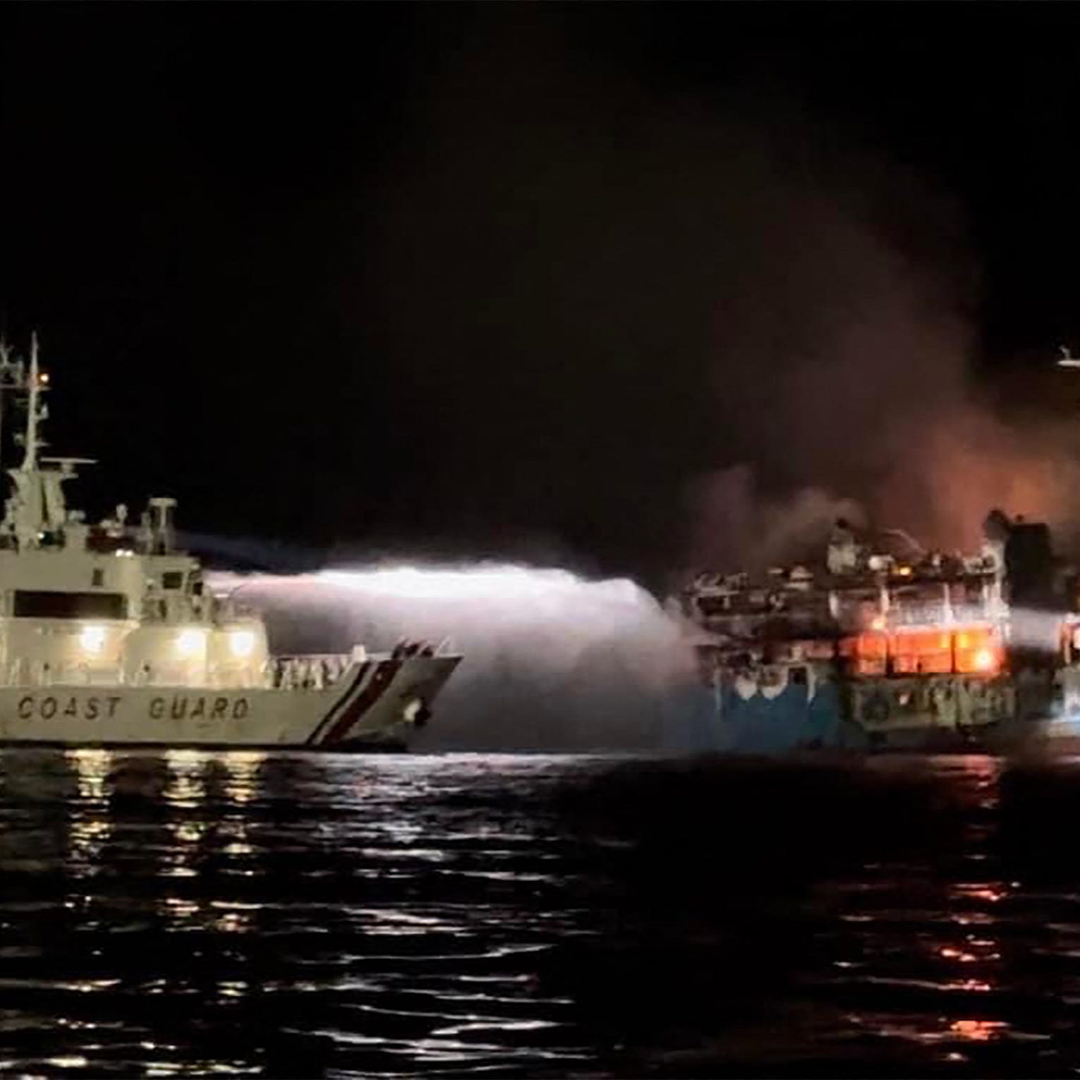 This handout picture taken on March 29, 2023 and released by the Philippine Coast Guard shows the Philippine Coast Guard spraying water on a fire onboard the Lady Mary Joy 3 during a search and rescue operation in waters off Baluk-Baluk Island in Basilan province. - At least 12 people died and 230 were rescued after a fire engulfed a ferry in the southern Philippines, authorities said on March 30.