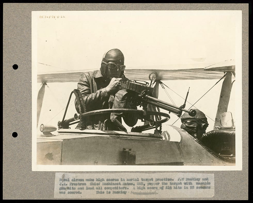 Photograph shows J.W. Buckley and J.A. Fenstrom, Chief Machinest Mates, U.S. Navy, as they "pepper the target with machine gun hits and lead all competitors. A high score of 214 hits in 53 seconds was scored." Buckley is shown operating the machine gun as Fenstrom flies the airplane.