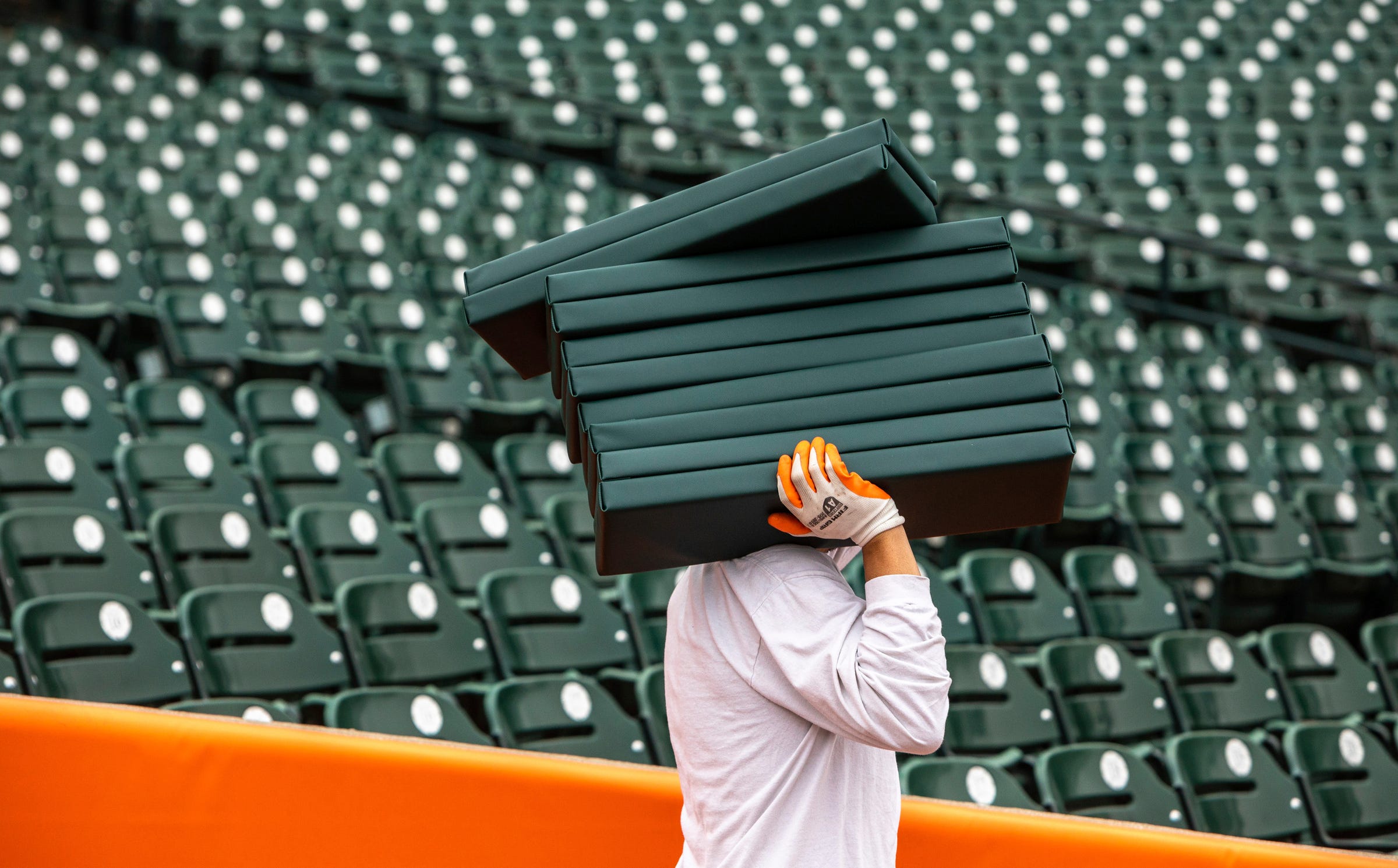 Alejandro Flores carries a stack of green cushions inside Comerica Park on Tuesday, April 4, 2023.