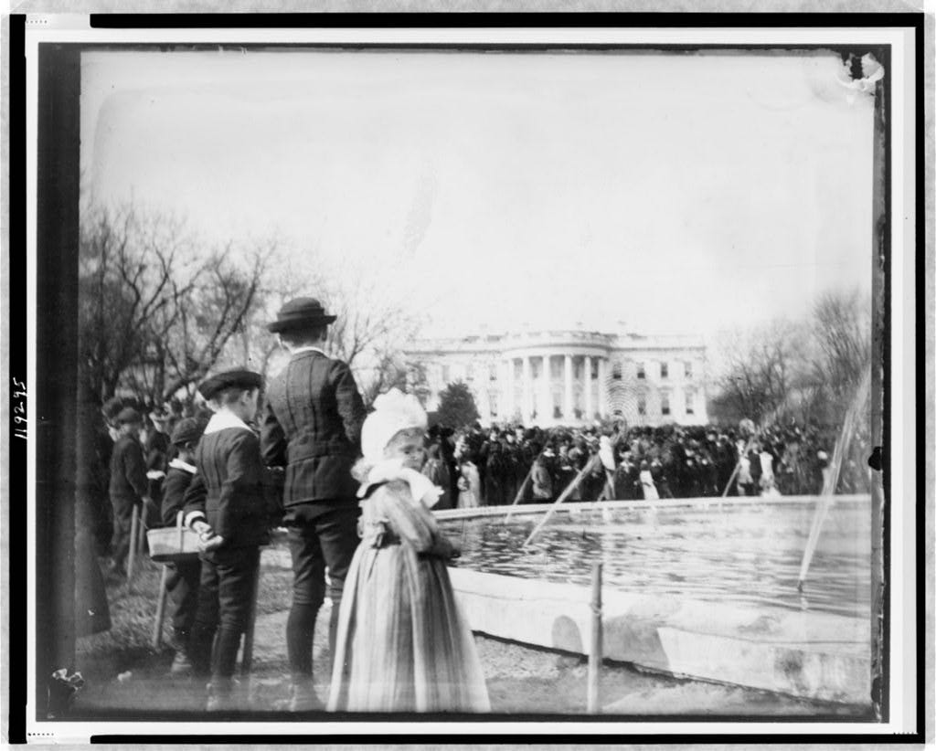 Crowd of people around pool, with the White House in background in 1889.