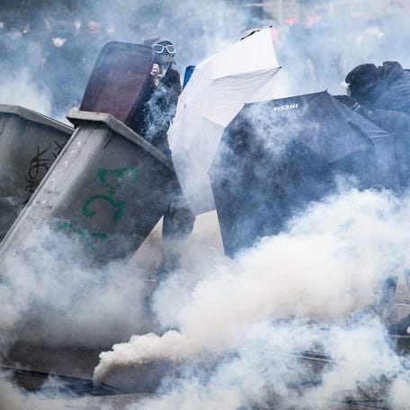 Protesters protect themselves from tear gas smoke behind umbrellas and garbage containers during clashes on the sidelines of a demonstration on the 11th day of action after the government pushed a pensions reform through parliament without a vote, using article 49.3 of the constitution, in Nantes, western France, on April 6, 2023. - France on April 6, 2023, braced for another day of protests and strikes to denounce the French President's pension reform one   day after talks between the government and unions ended in deadlock.