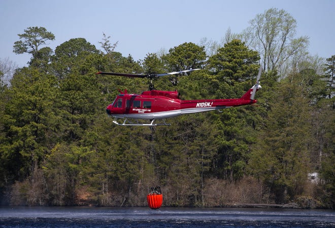 A helicopter from New Jersey State Forest Fire Service helps to fight the fire. It refills with water at Lake Horicon. First responders battle the “Jimmy’s Waterhole Fire” early in the day. The fire raged overnight threatening structures but firefighters have made progress in extinguishing the blaze.Lakehurst, NJWednesday, April 12, 2023