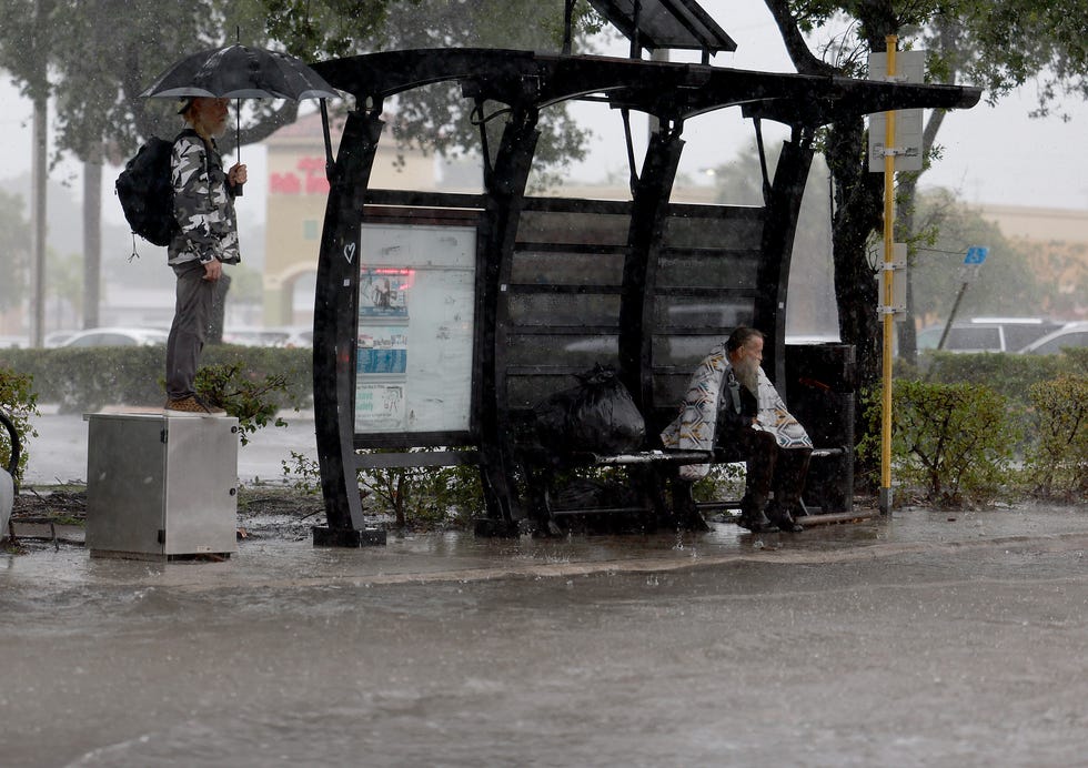 People wait for a bus next to a flooded road on April 12, 2023, in Dania Beach, Florida. Heavy rain passed through the South Florida area causing some area flooding.