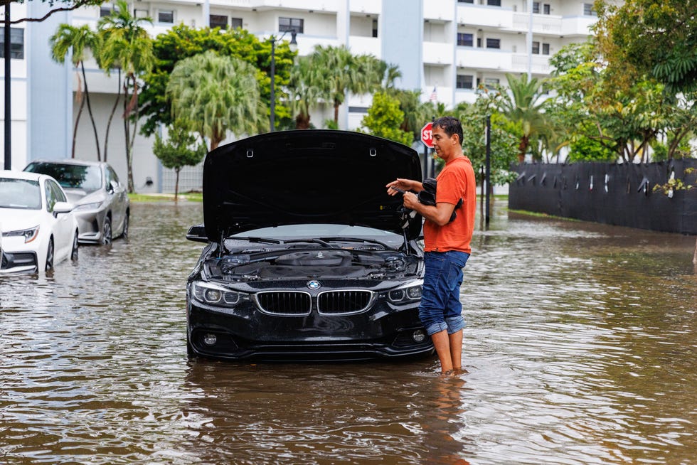 A person stands next to his vehicle stranded on a flooded road due to heavy rain at North Bay Rd. and 179th Dr. in Sunny Isles Beach, Fla., on Wednesday, April 12, 2023.