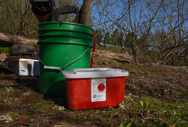 A sharps container for collected syringes and needles join's a bucket of tools gathered during a cleanup of an island camping site in the Willamette River.