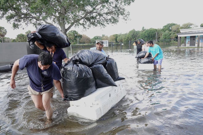 Menschen versuchen, Wertsachen zu retten, während sie am Donnerstag, den 13. April 2023, durch Hochwasser um Fort Lauderdale, Florida, waten.