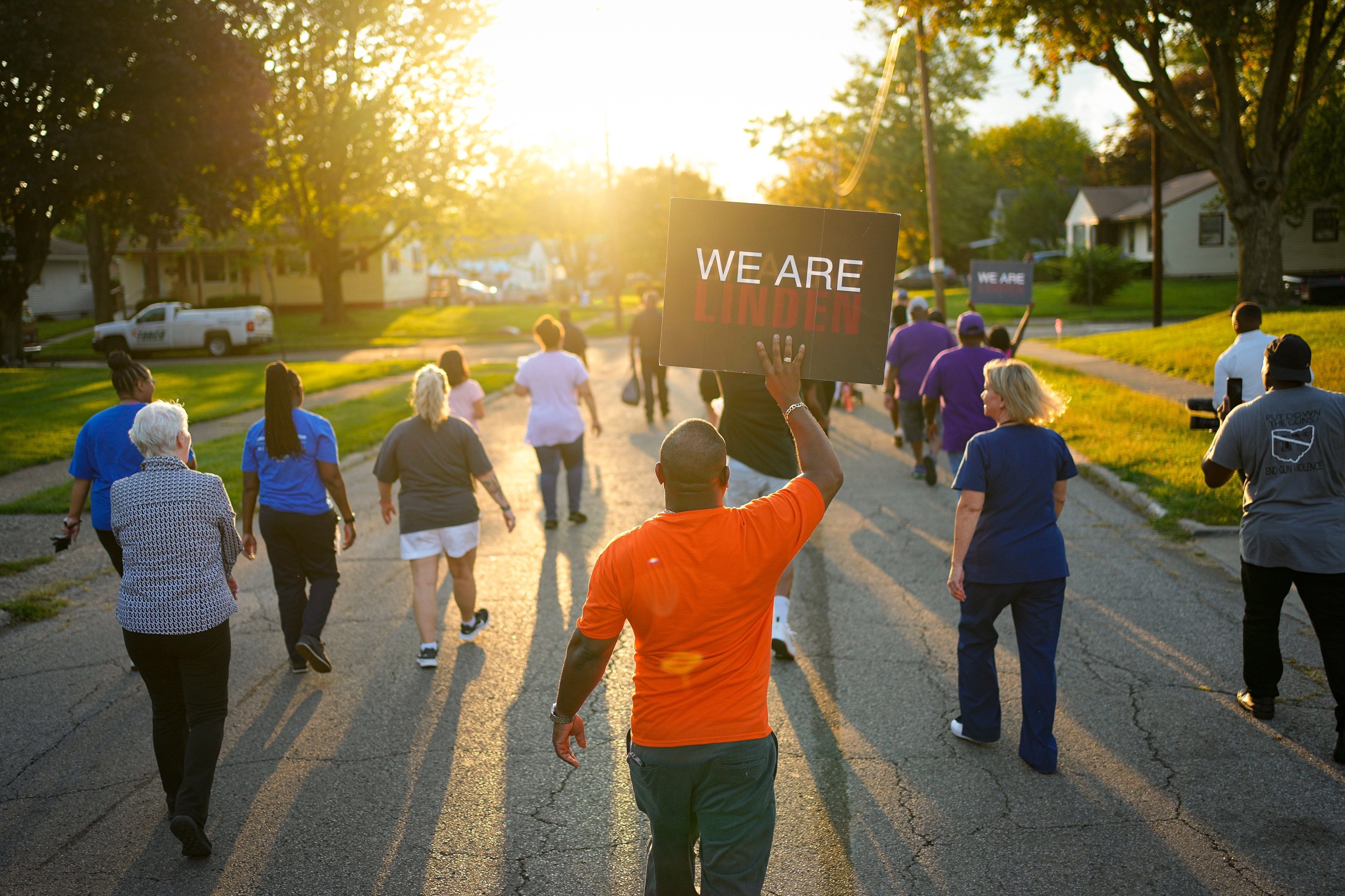 Dana Brock carries a "We Are Linden" sign as organizers from the community visit a neighborhood behind the Northern Lights Shopping Center on Sept. 19 cheering on local residents with messages about stopping gun violence and bringing the Linden community together.