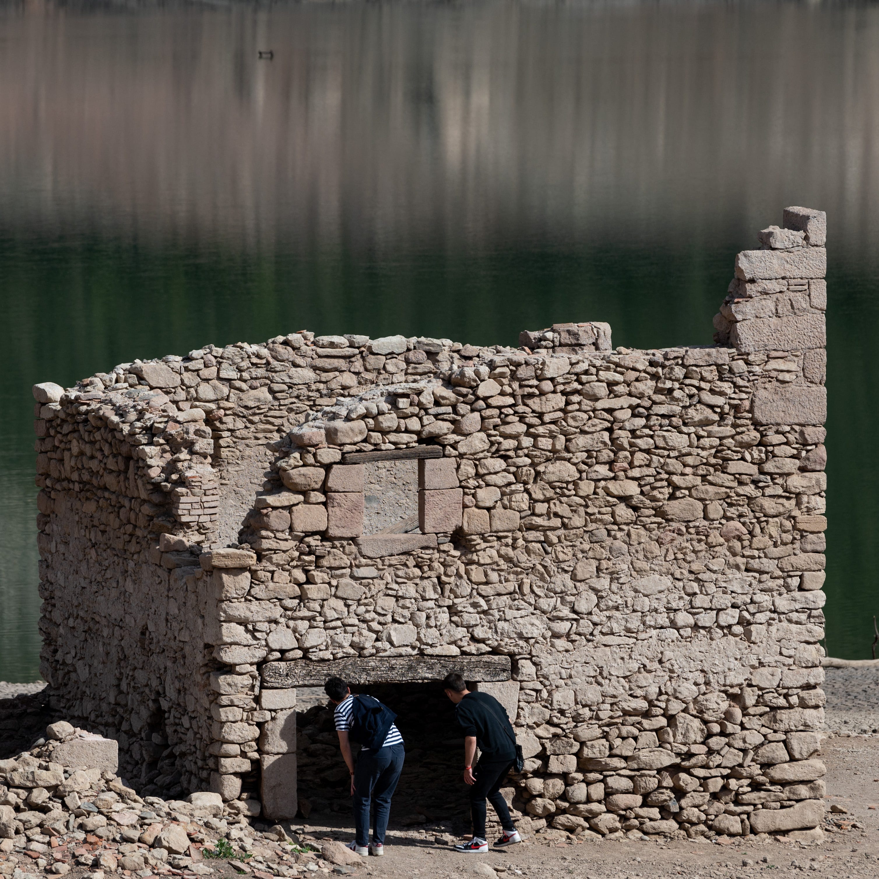 People look into a ruined house of Sant Roma de Sau on the dried banks of the swamp of Sau, located in the province of Girona in Catalonia on April 16, 2023.