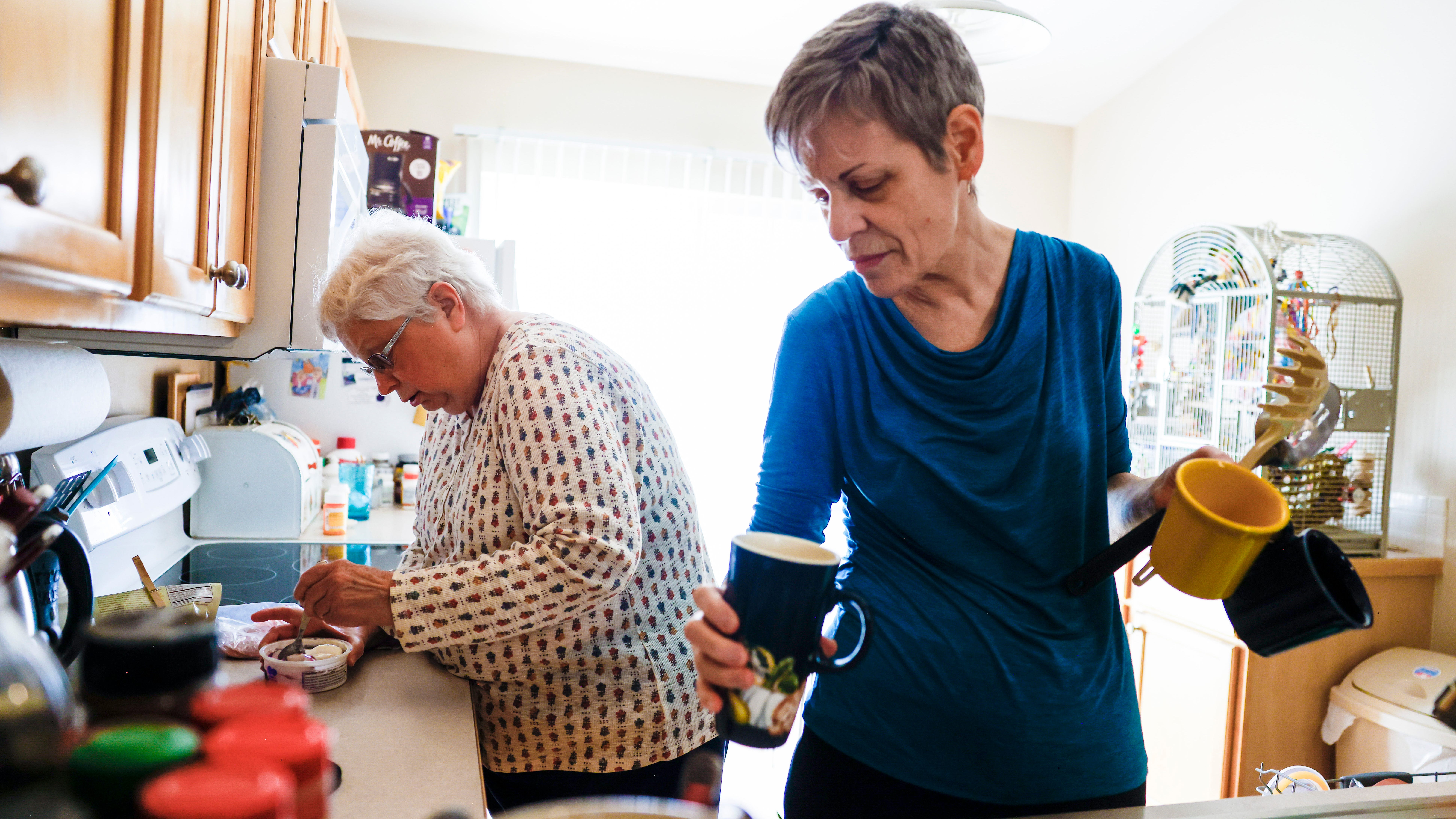Marlene Mears, right, puts away dishes while Becky Miller, left, prepares food in their kitchen in Longmont, Colo.