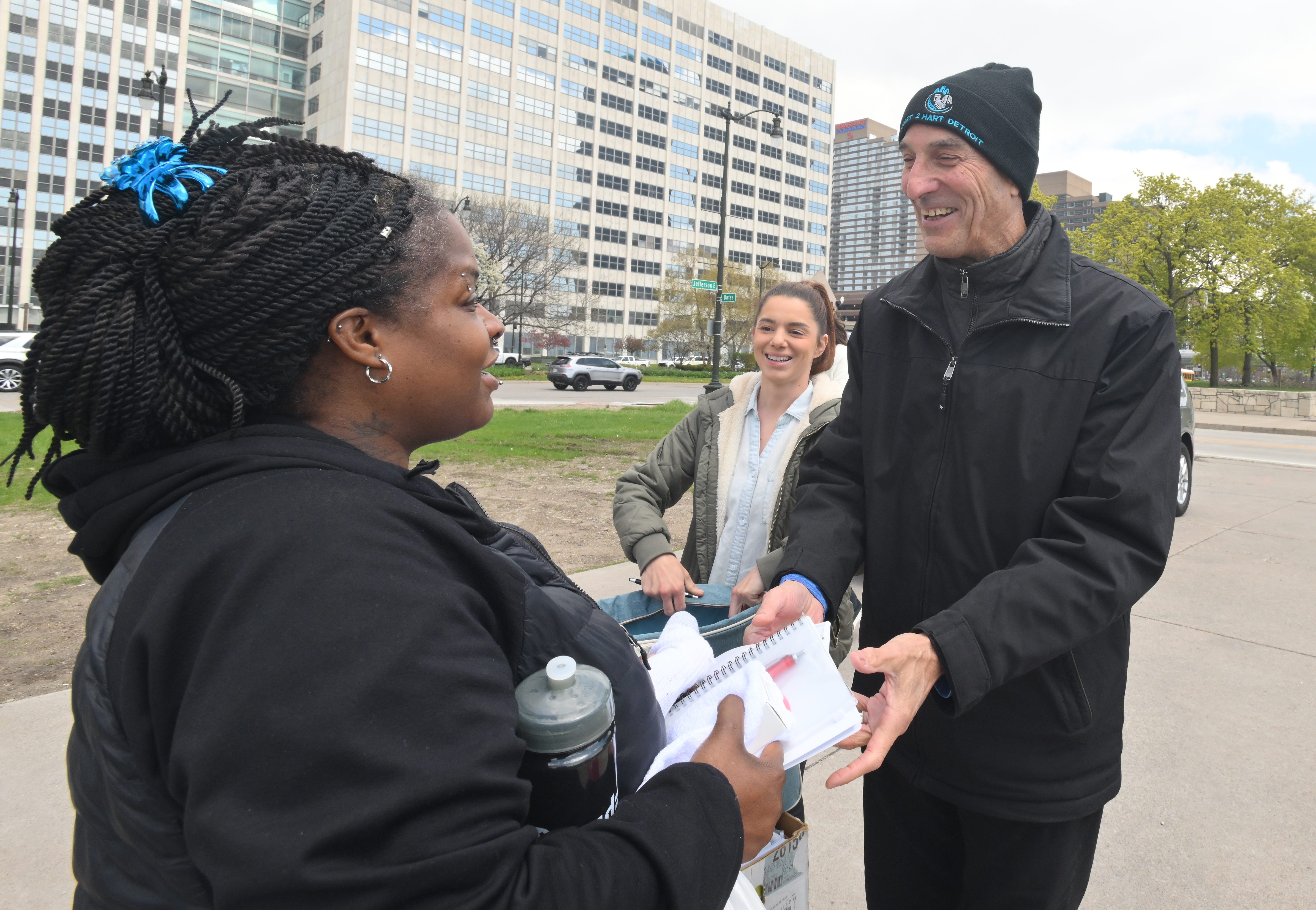 Marcia Hardy picks up some supplies and a lunch from Larry Oleinick, founder and president of Heart 2 Hart Detroit, and Melissa Newton in Detroit's Hart Plaza on April 26, 2023.