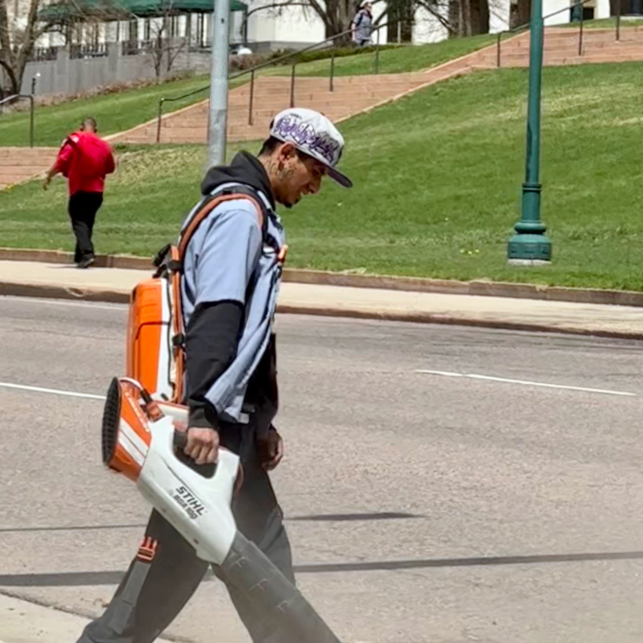 A worker uses a battery-powered leaf blower to  clean gutters in Denver, Colorado. Some regulators are considering limiting the sale and use of gas-powered lawn equipment in the Denver area to improve air quality.