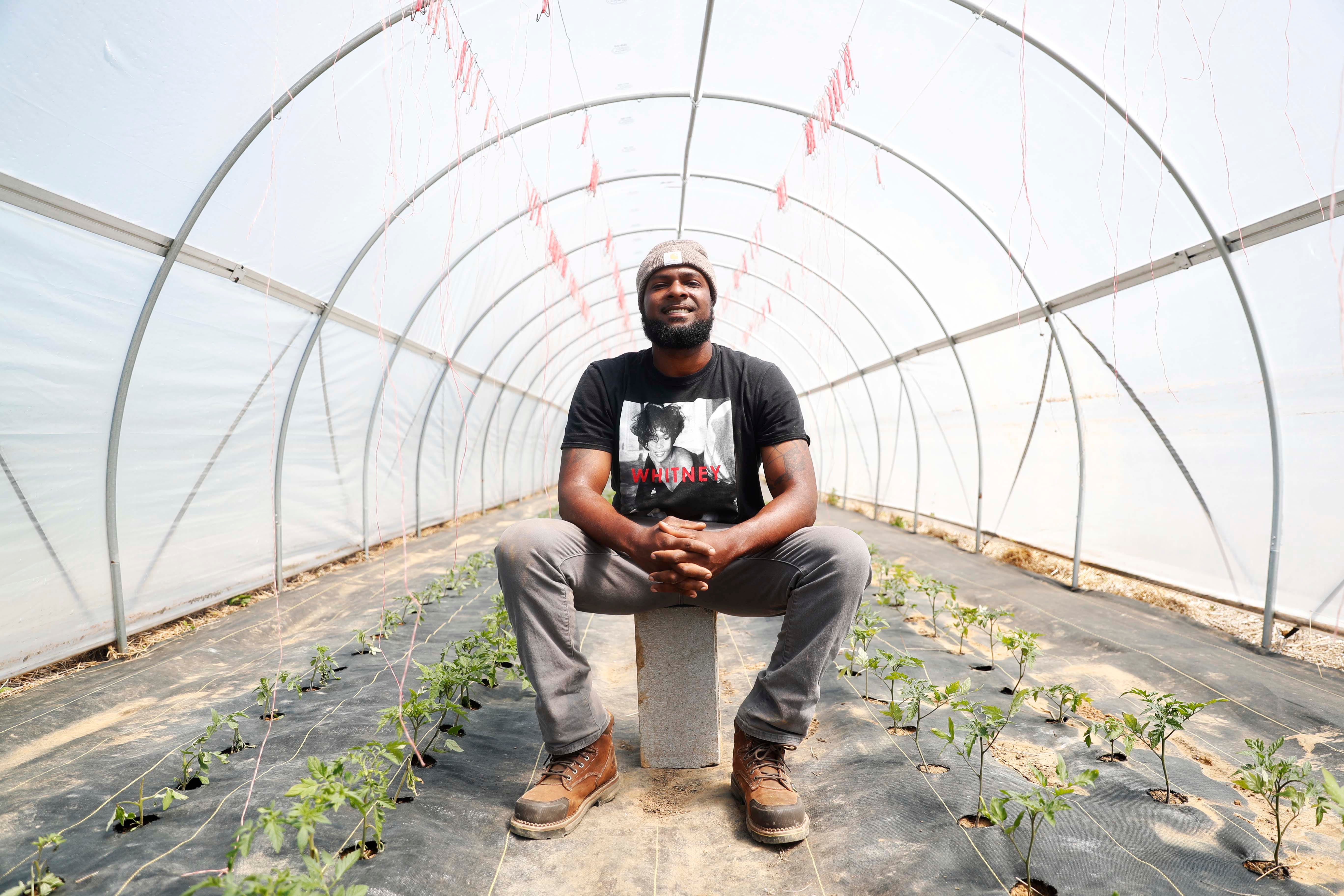 Matthew Robinson, a young farmer, poses in front of planted tomatoes in his hoop house type greenhouse at his farm in Stanton, Tennessee, on May 3, 2023.
