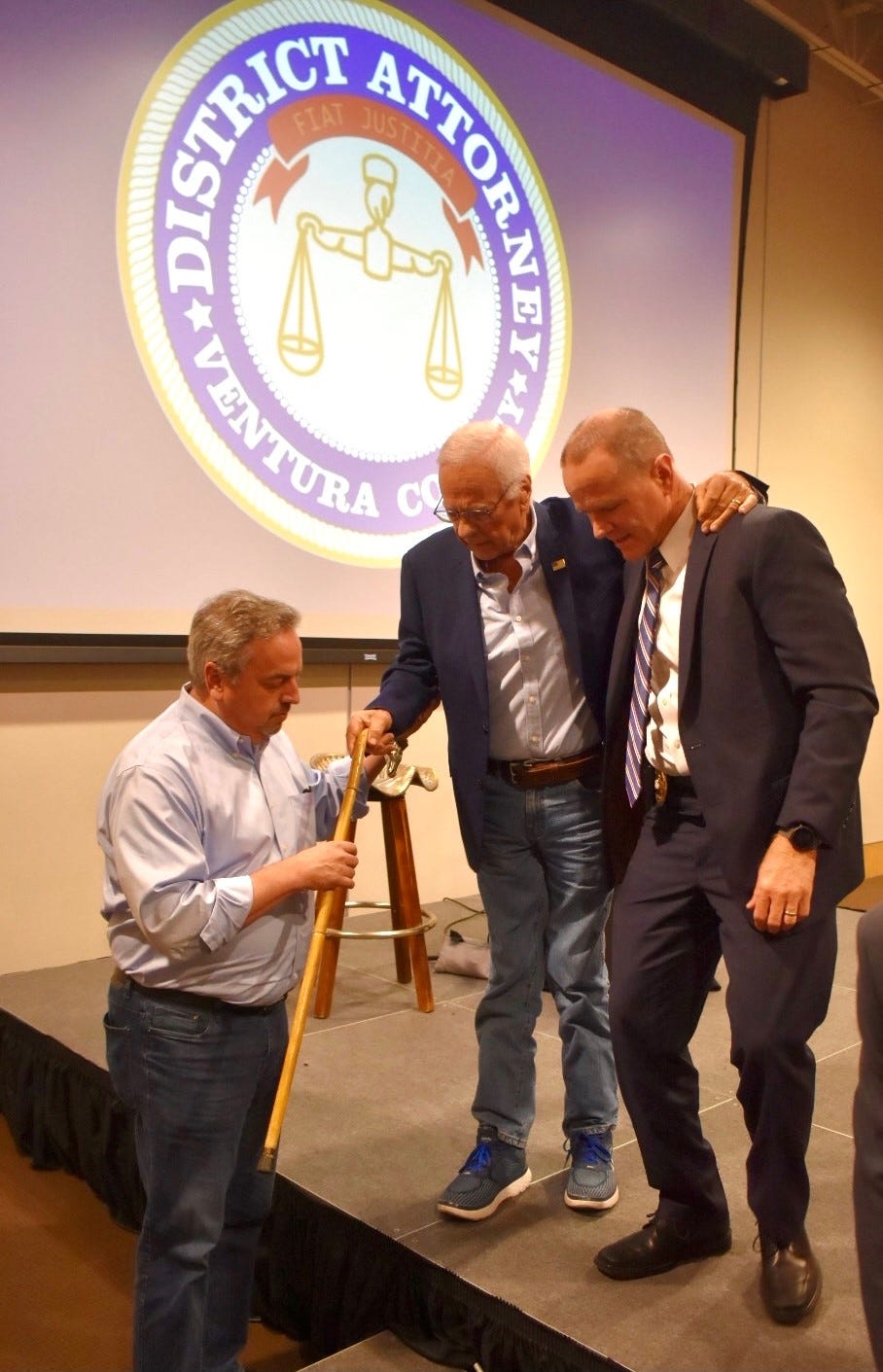Former District Attorney Mike Bradbury is helping off the stage after a program at the Museum of Ventura County on May 3. Bradbury was diagnosed 20 years ago with a muscle deterioration disease called myositis.
