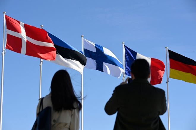 Люди стоят перед финским национальным флагом (в центре) после церемонии поднятия флага в штаб-квартире НАТО в Брюсселе, вторник, 4 апреля 2023 года. Финляндия стала 31-м членом НАТО, завершив свой исторический стратегический переход депозитом.  документы о присоединении к коалиции.  (Джон Тиз/AFP/Getty Images/TNS)