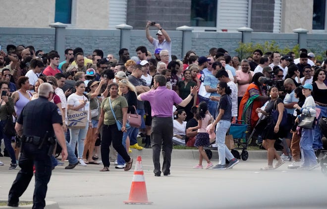 People gather across the street from a shopping center after a shooting Saturday, May 6, 2023, in Allen, Texas.