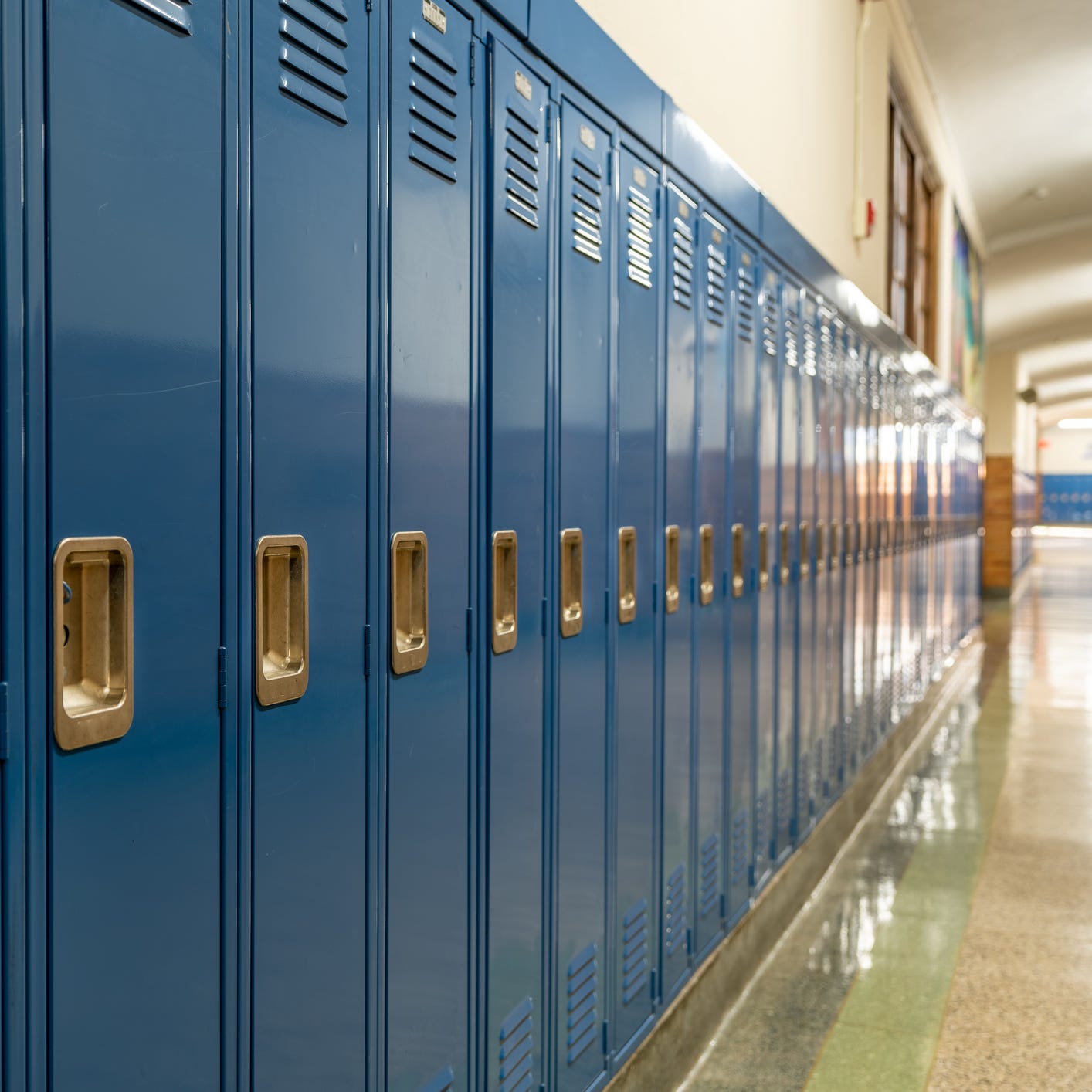 Photo of a blue metal lockers along a nondescript hallway in a typical US High School. No identifiable information included and nobody in the hall.