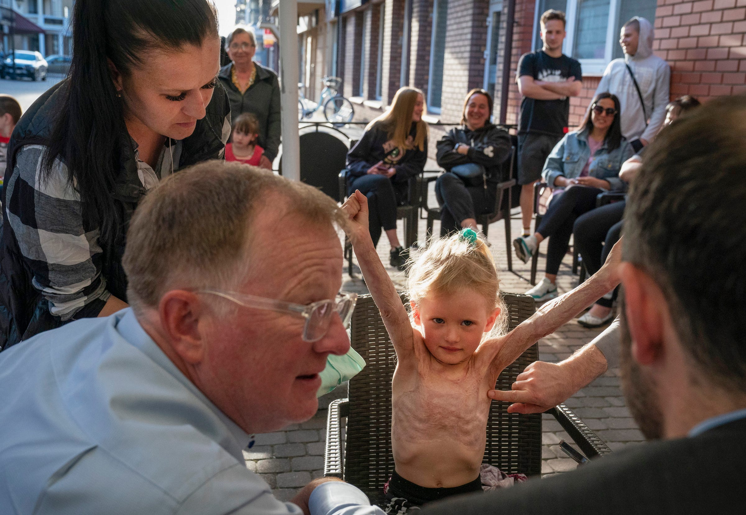 Ludmila Nativa, 31, of Mykolaiv, Ukraine looks on from left as her niece Yelizaveta Nadolniak, 4, is screened by Dr. David Brown, a plastic surgeon from the University of Michigan, lower left, and Dr. Brian Kelley, a plastic surgeon at the University of Texas at Austin Dell Medical School  Sunday, May 14, 2023 at a hotel in Leczna, Poland. Nadolniak was burned in a house fire in the winter of 2022 and needs surgery on her scar tissue to be able to move her arms.