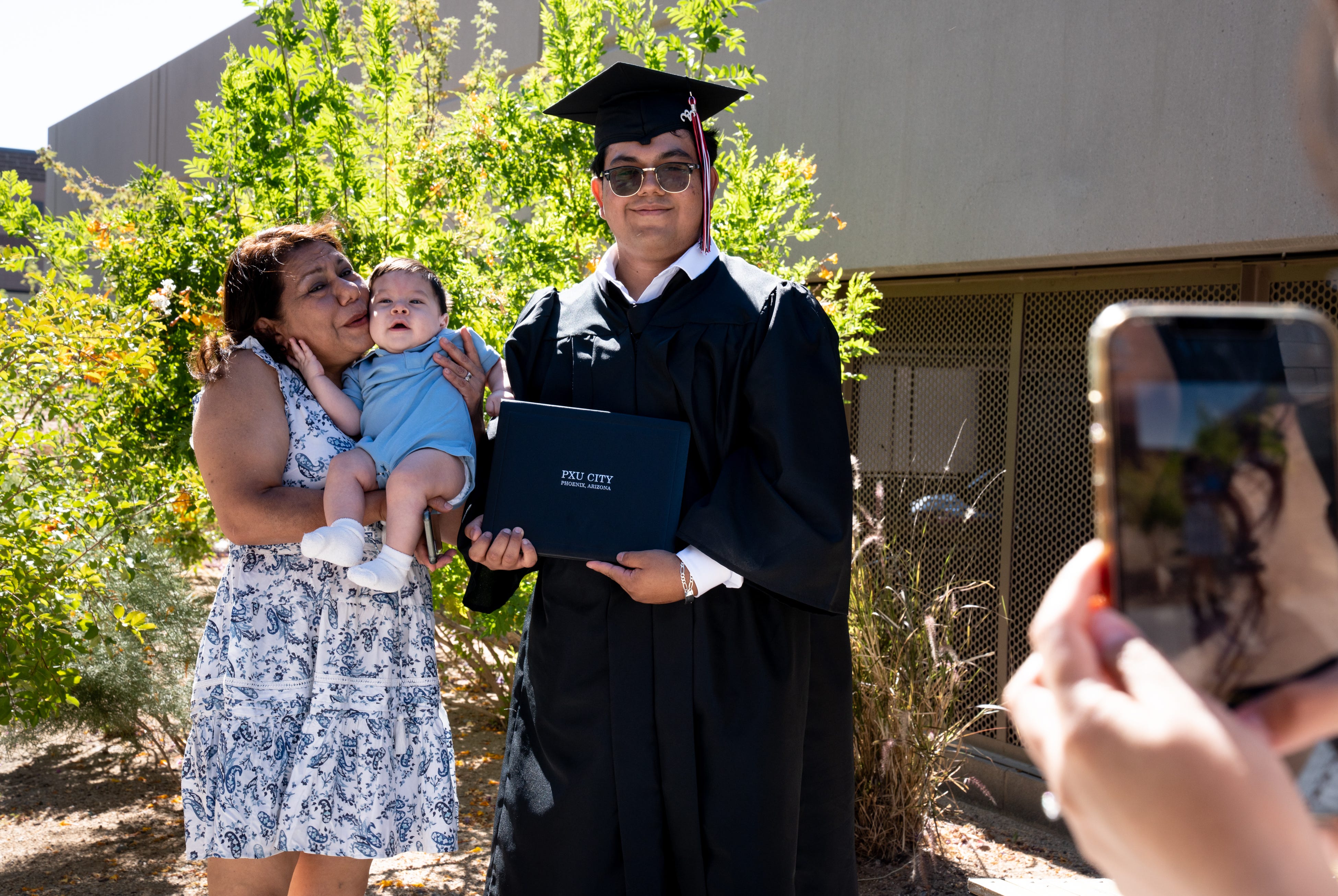 PXU City student Ali Gonzalez (right) has his photo taken with his mom, Silvia Choperena (left) and his nephew, Lukia Gonzalez (center), on May 24, 2023, after his graduation ceremony at the Madison Center for the Arts in Phoenix.