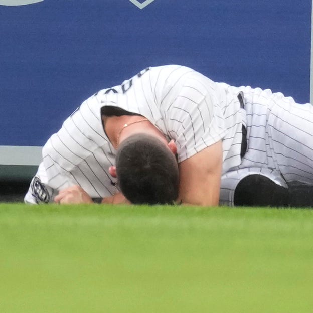 Colorado Rockies center fielder Brenton Doyle lies on the warning track after running into the wall while pursuing a home run by the Miami Marlins' Jorge Soler.