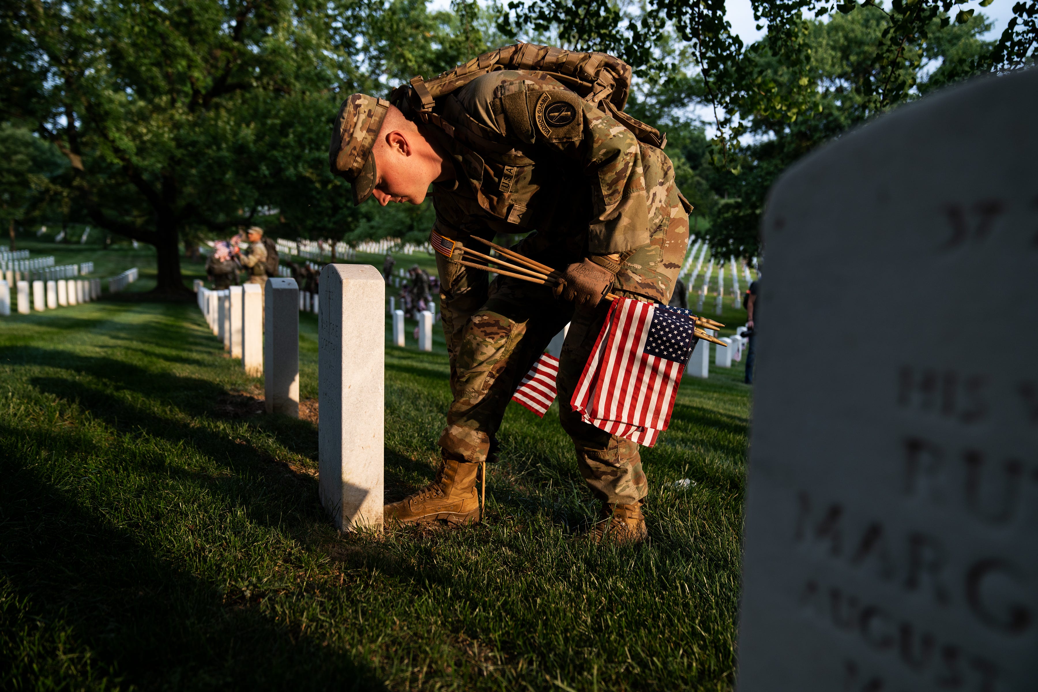 A member of the 3rd U.S. Infantry Regiment places a flag into the ground, exactly one boot length from the headstone's base during a joint service “Flags-In” ceremony at Arlington National Cemetery on Thursday, May 25, 2023.