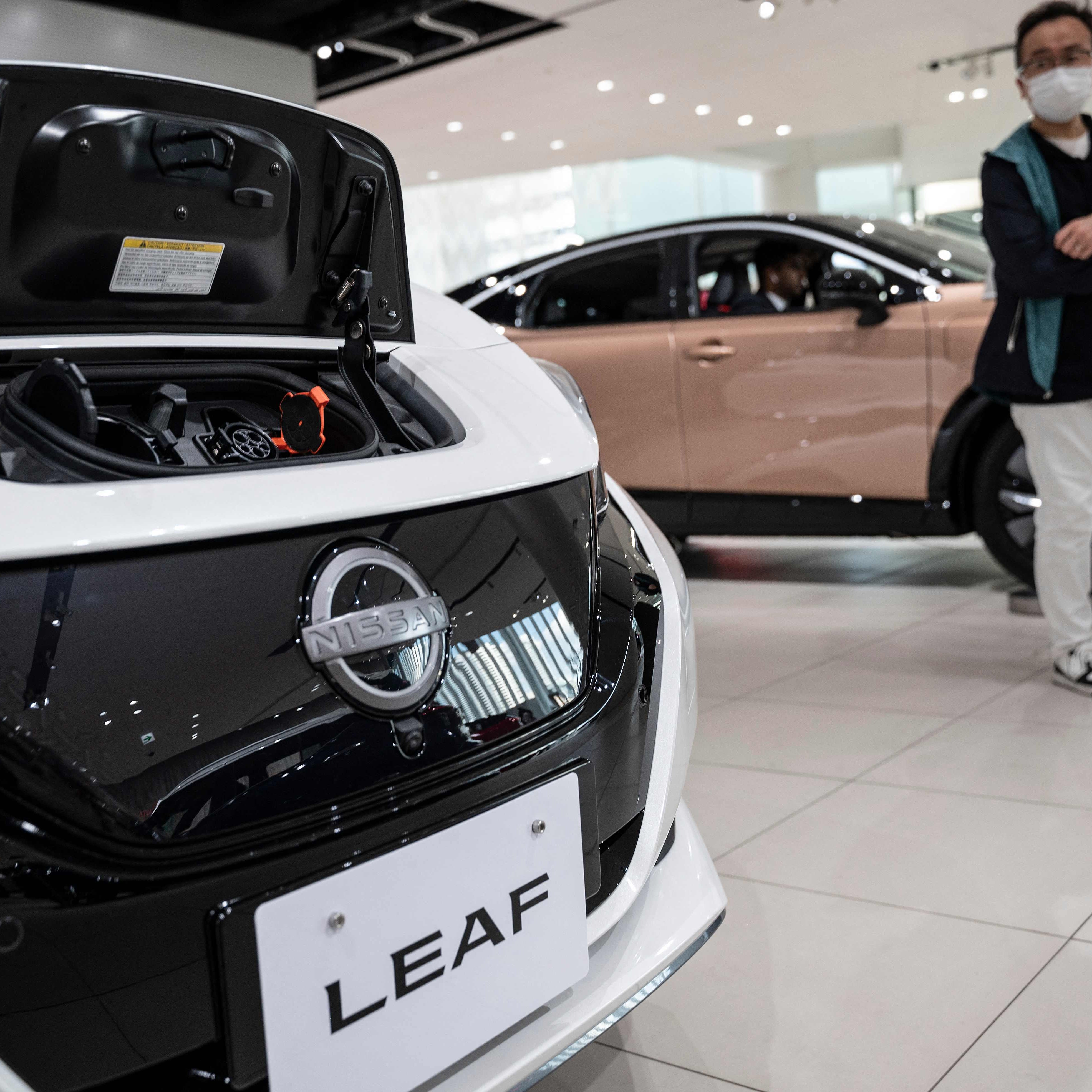 This photo taken on March 30, 2023 shows a man walking past one of Nissan's electric vehicles (EV), the Leaf, at the global headquarters of Japanese automaker Nissan Motor in Yokohama, Kanagawa prefecture.