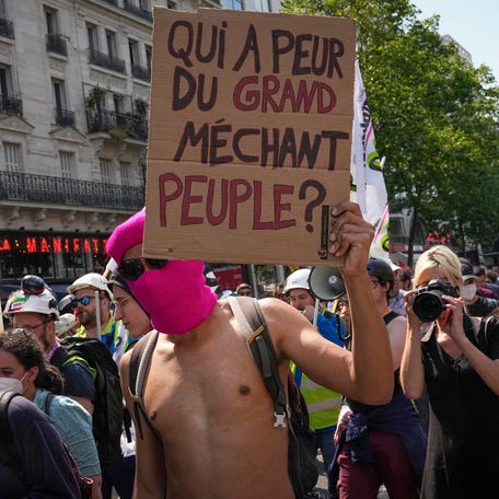 A man holds a placard with the slogan "Who is afraid of the big nasty people?" during a protest in Paris, France, Tuesday, June 6, 2023. French unions are seeking to reignite resistance to President Emmanuel Macron's higher retirement age with what may be a final surge of nationwide protests and scattered strikes Tuesday.