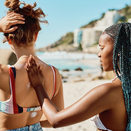 Shot of a young woman applying sunscreen to her friend's back on the beach.