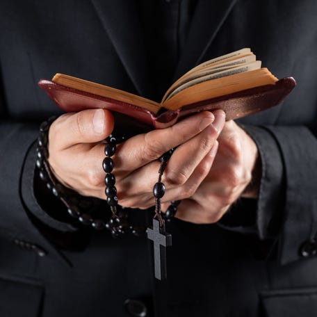 Religious person studies Bible and holds prayer beads, low-key image