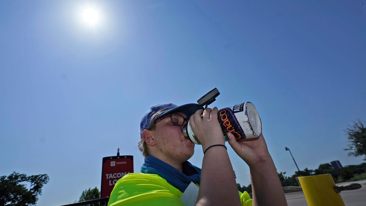 Jennifer Michener drinks water while working in the hot sun in a parking lot in Arlington, Texas, Monday, June 26, 2023.