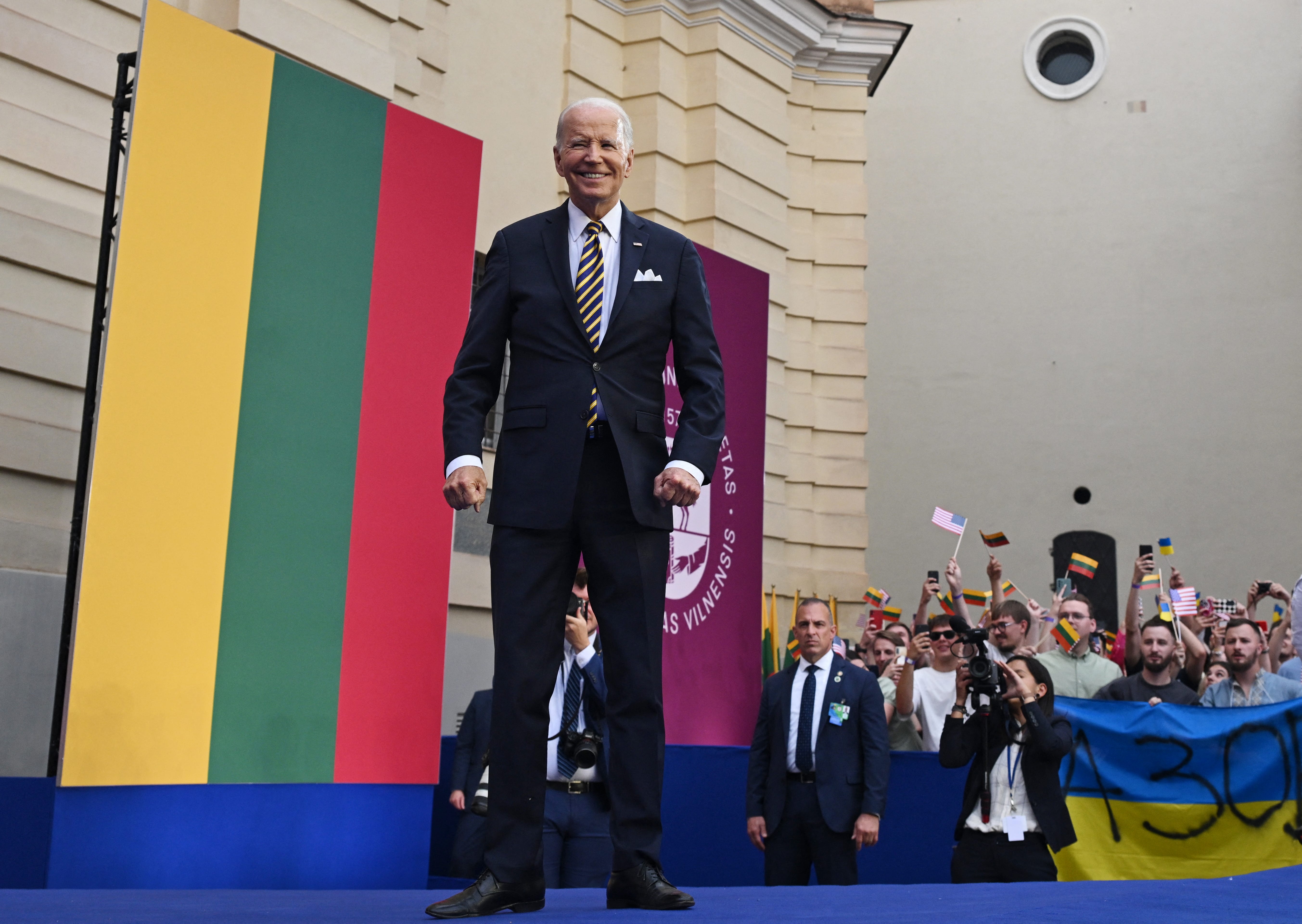 US President Joe Biden reacts during his speech on NATO and people cheer with flags in the background at the Vilnius University in Vilnius, Lithuania, on July 12, 2023, after the end of the NATO Summit.