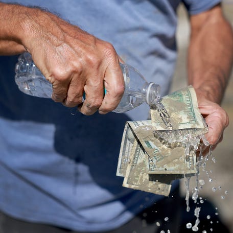 FORT MYERS, FLORIDA - OCTOBER 01: James Pironti washes off the muddy money he recovered from his bedroom after Hurricane Ian passed through the area on October 1, 2022 in Fort Myers, Florida.  The Category 4 hurricane brought high winds, storm surge and rain to the area causing severe damage. (Photo by Joe Raedle/Getty Images)
