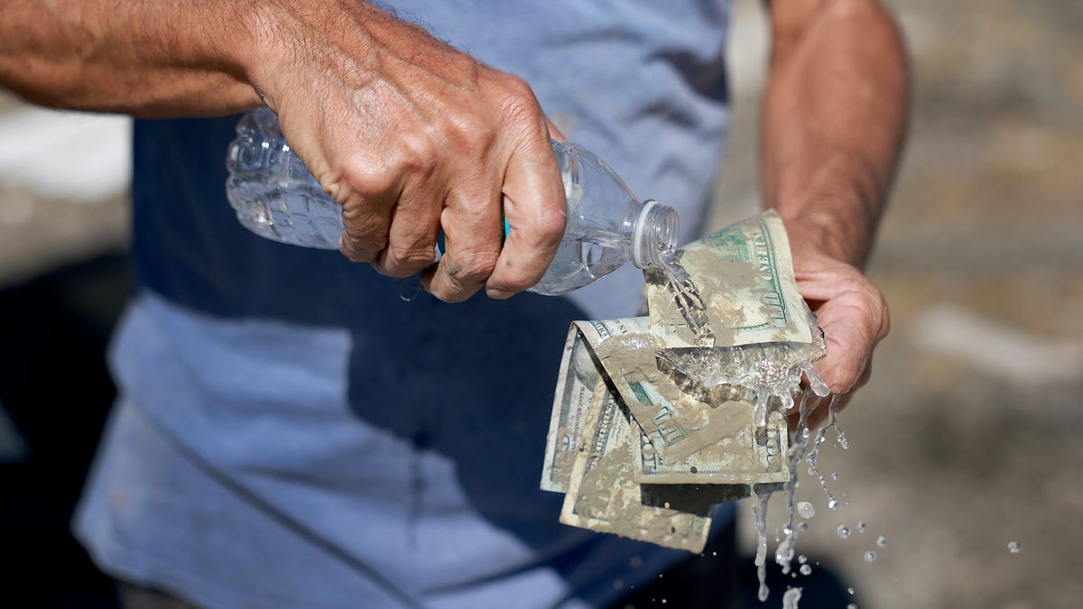 FORT MYERS, FLORIDA - OCTOBER 01: James Pironti washes off the muddy money he recovered from his bedroom after Hurricane Ian passed through the area on October 1, 2022 in Fort Myers, Florida.  The Category 4 hurricane brought high winds, storm surge and rain to the area causing severe damage. (Photo by Joe Raedle/Getty Images)