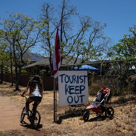 A girl rides her bike past a sign that says "Tourist Keep Out," in Lahaina, Hawaii, Thursday, Aug. 17, 2023. Long before a wildfire blasted through the island of Maui the week before, there was tension between Hawaii's longtime residents and the visitors some islanders resent for turning their beaches, mountains and communities into playgrounds. But that tension is building in the aftermath of the deadliest U.S. wildfire in more than a century. (AP   Photo/Jae C. Hong)