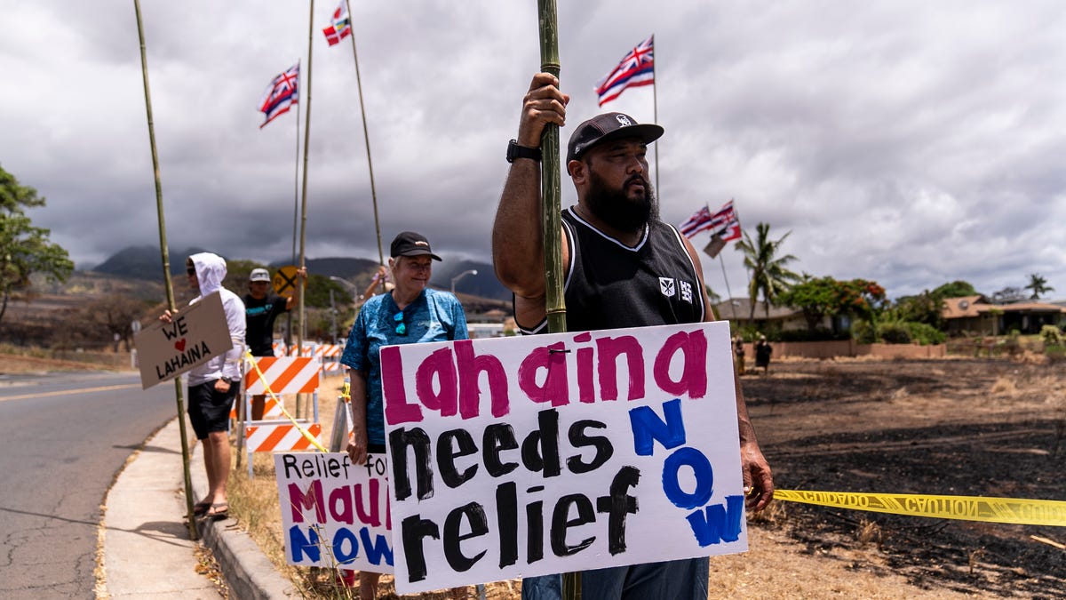 Dustin Pilialoha stands with a sign while waiting for the arrival of President Joe Biden outside the Lahaina Civic Center in Lahaina, Hawaii, Monday, Aug. 21, 2023. (AP Photo/Jae C. Hong) ORG XMIT: HIJH107