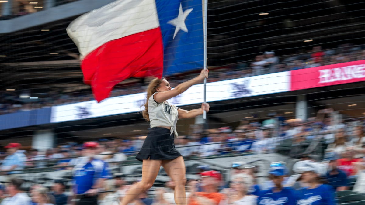 A member of the Texas Rangers Six Shooters Squad carries a Texas flag atop the visitors dugout before a baseball game between the Texas Rangers and the Los Angeles Dodgers Saturday, July 22, 2023, in Arlington, Texas. Los Angeles won 16-3.